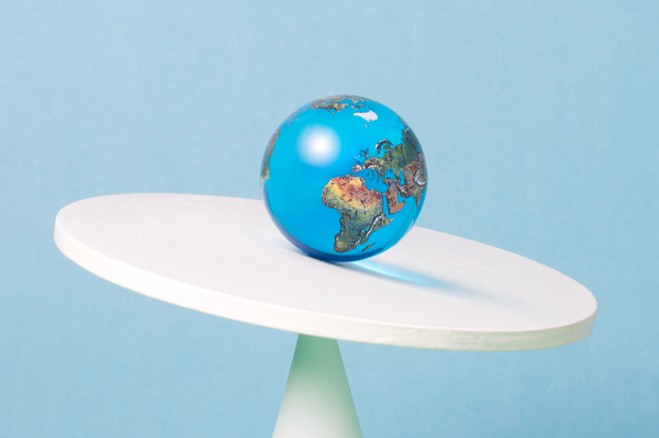 A globe sits on a tilted round white disc atop a white cone against a light blue background