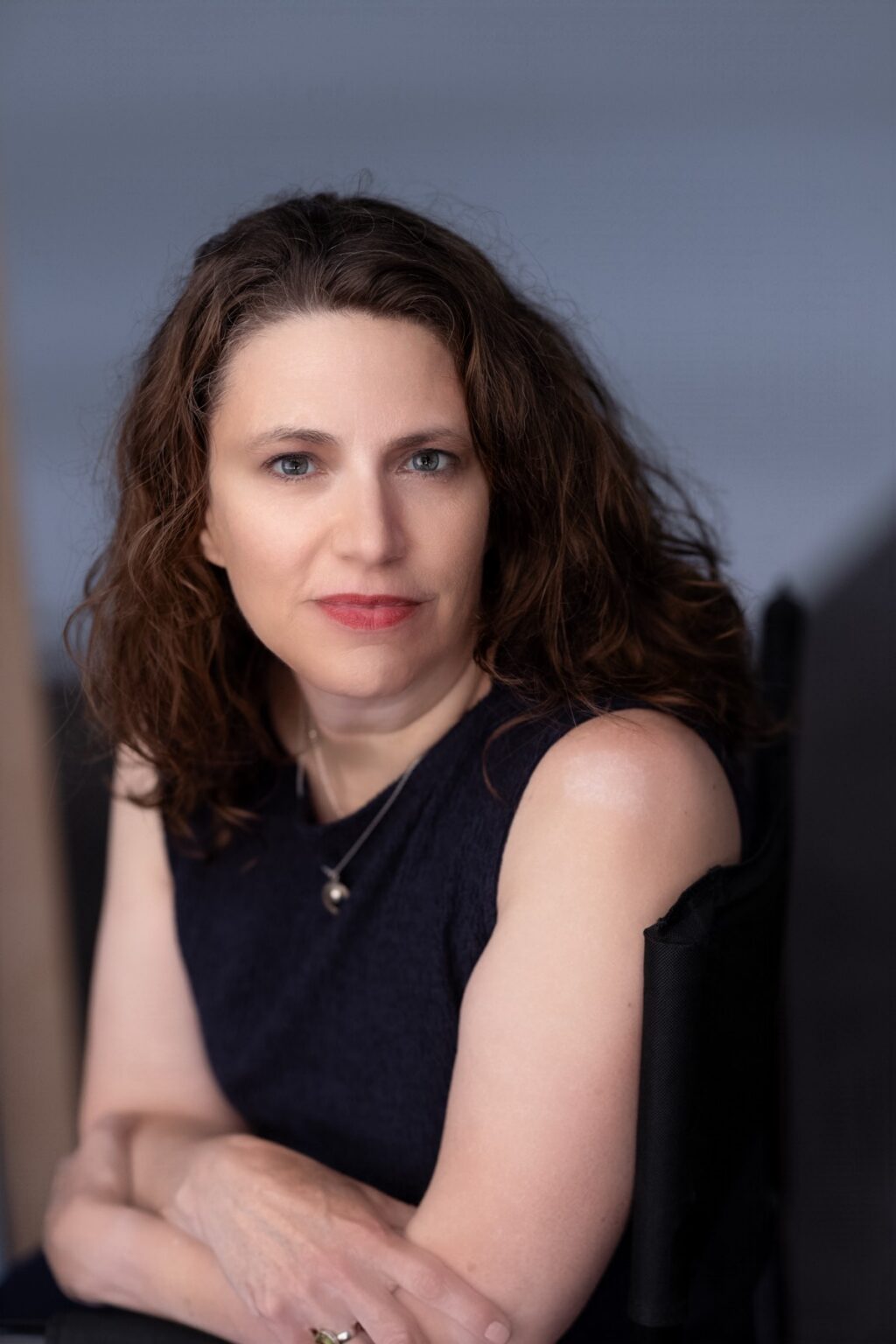 Portrait style author photo featuring young woman with long curly brown hair wearing a black sleeveless top