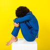 Art creative installation single Black woman sitting in studio in blue suit on yellow background. The image illustrates the idea of hurting your own feelings by taking everything personally.