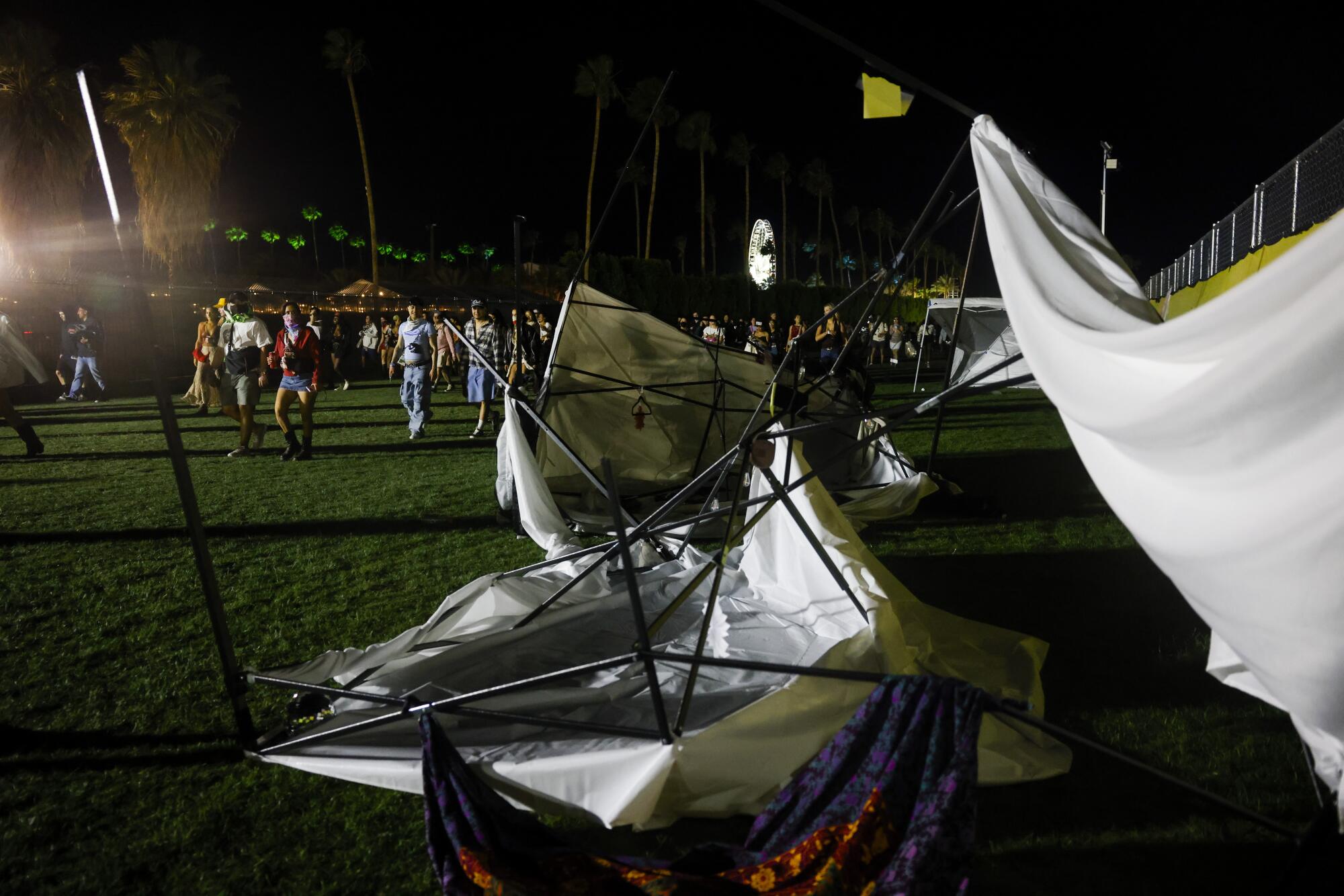 Festival goers walk past tents blown down by the wind.