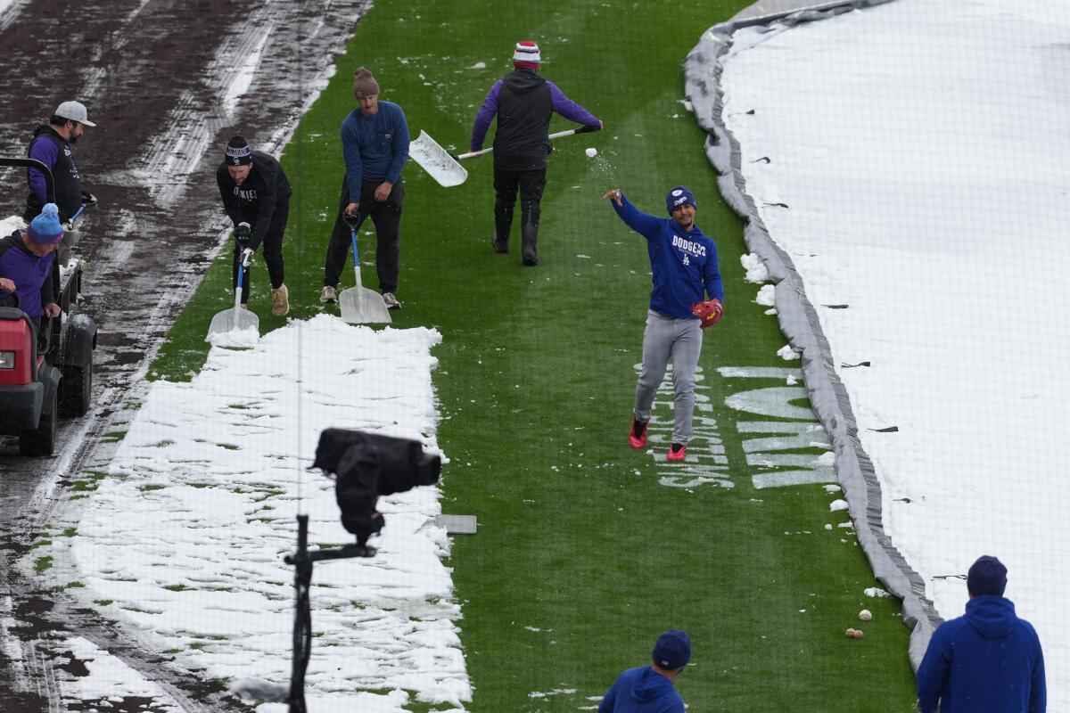 As the grounds crew works to clear snow while Dodgers third baseman Santiago Espinal tosses a snowball at a coach.