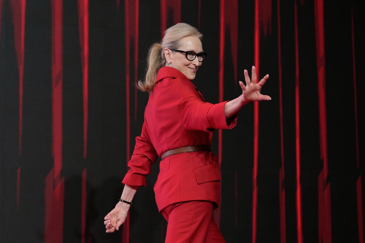 Meryl Streep, wearing a red power suit, waves at fans.