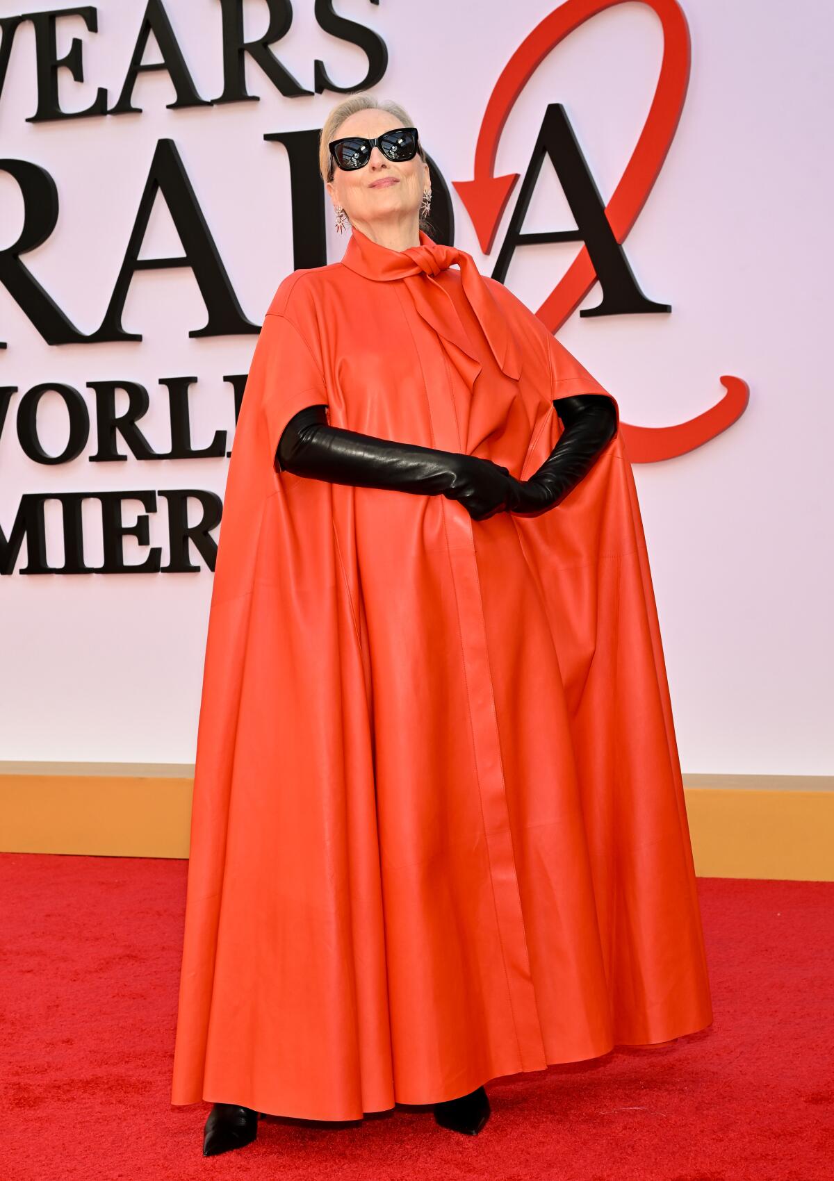 Meryl Streep wears a red cape dress, black gloves and black sunglasses on the red carpet. 