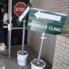 A sign that says "Measles Clinic" is shown. Two people are entering the Andrews County Health Department in Texas.