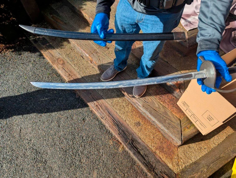 A man, seen from the waist down, holds a sword and sheath in either hand.