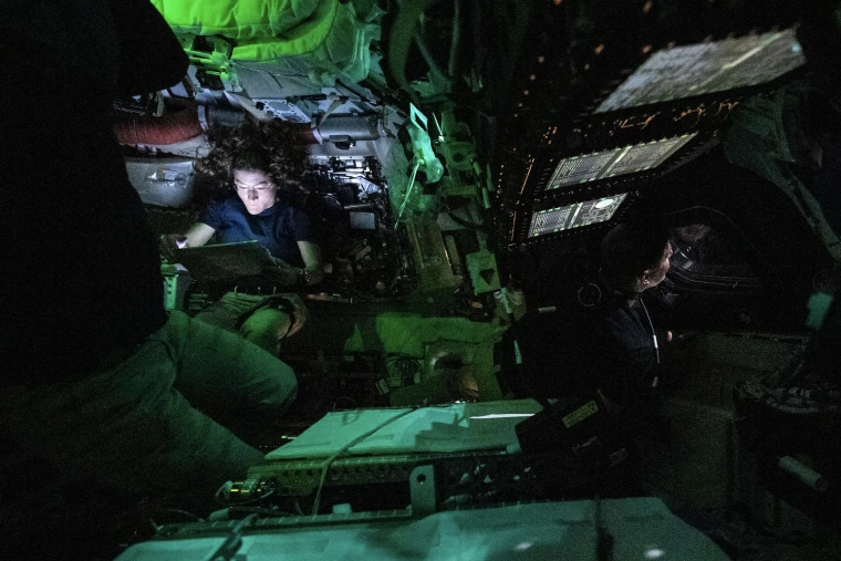 A darkened space shuttle capsule with two astronauts inside it.