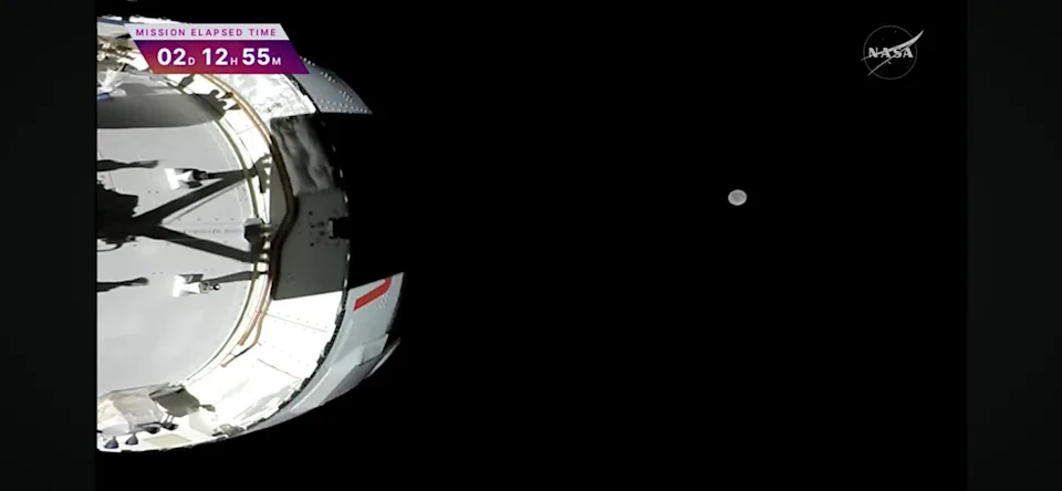 A camera on the end of an Orion solar wing shows the spacecraft and its target -- the moon -- suspended in black of deep space. / Credit: NASA