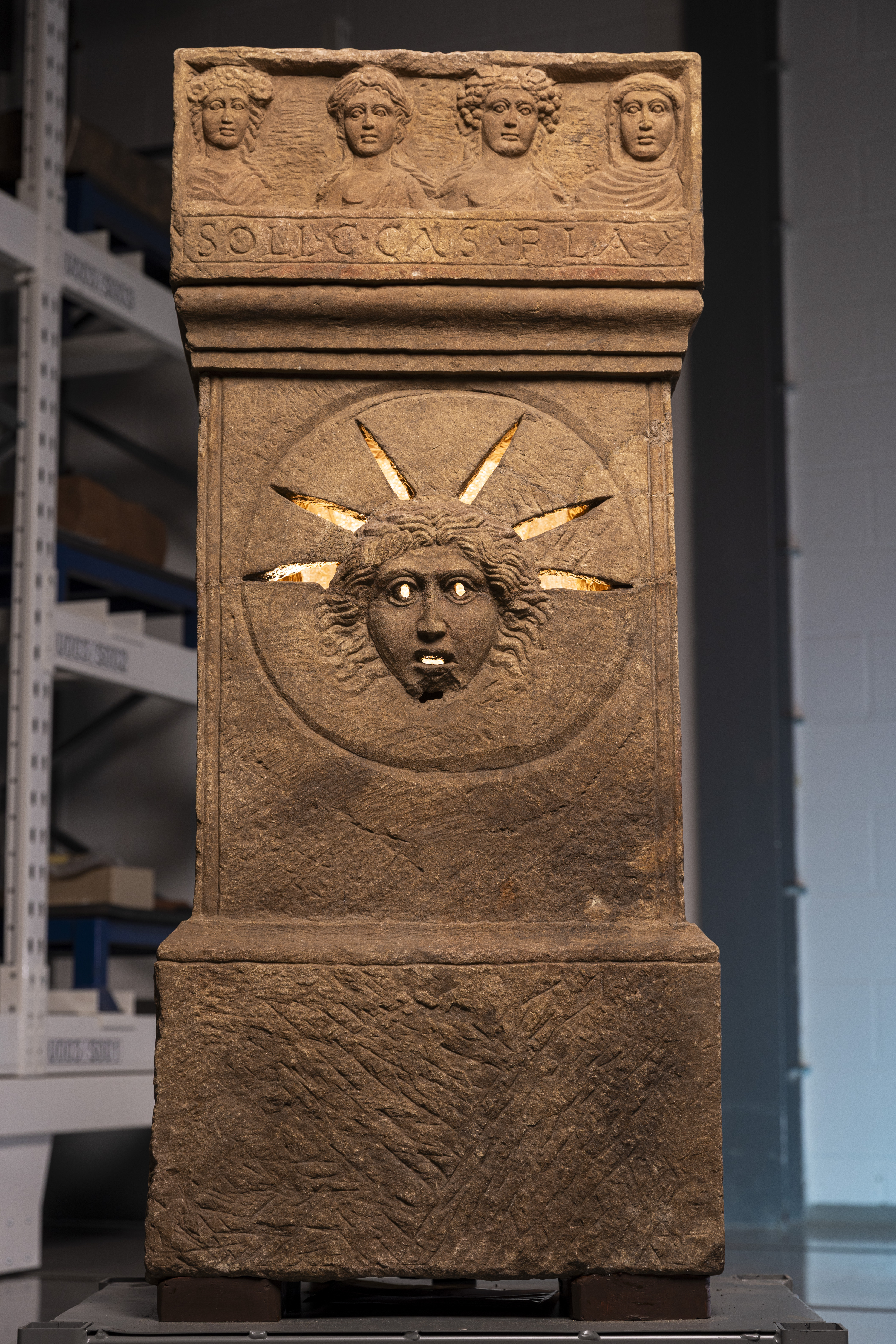 a stone altar carved with a humanlike face with rays coming out around the crown