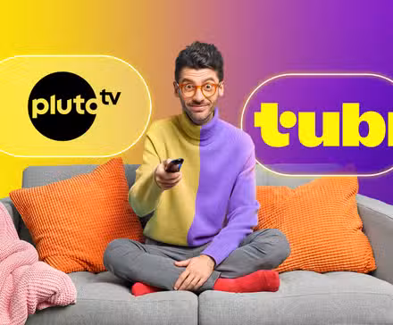 A guy on his couch holding the TV remote with the logos of Pluto TV and Tubi beside him.