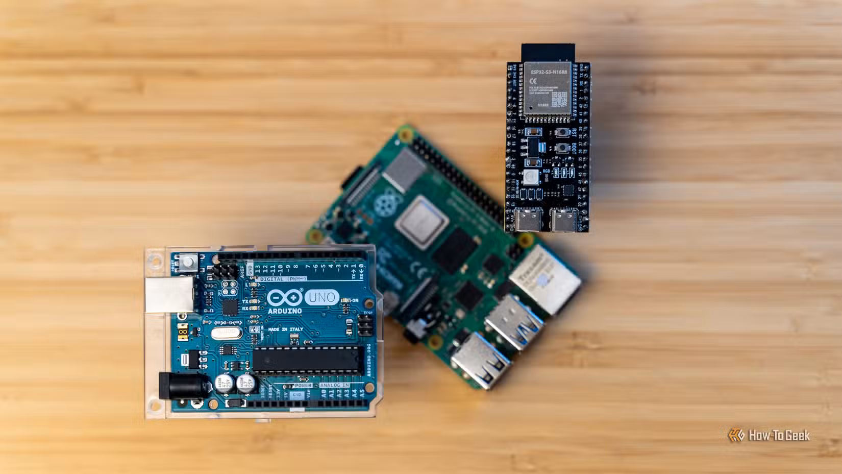 An Arduino Uno R3 and ESP32 floating above a Raspberry Pi on a wooden background.