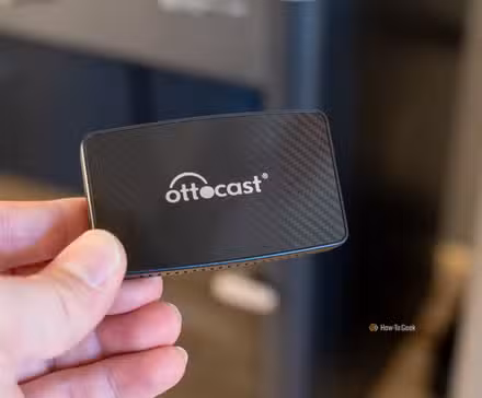 The Ottocast wireless CarPlay adapter being held in a hand.