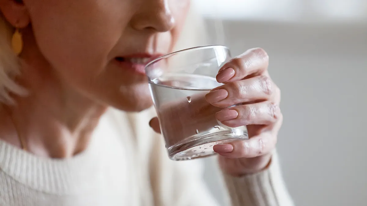 Senior woman holding a glass of water and raising it to her lips