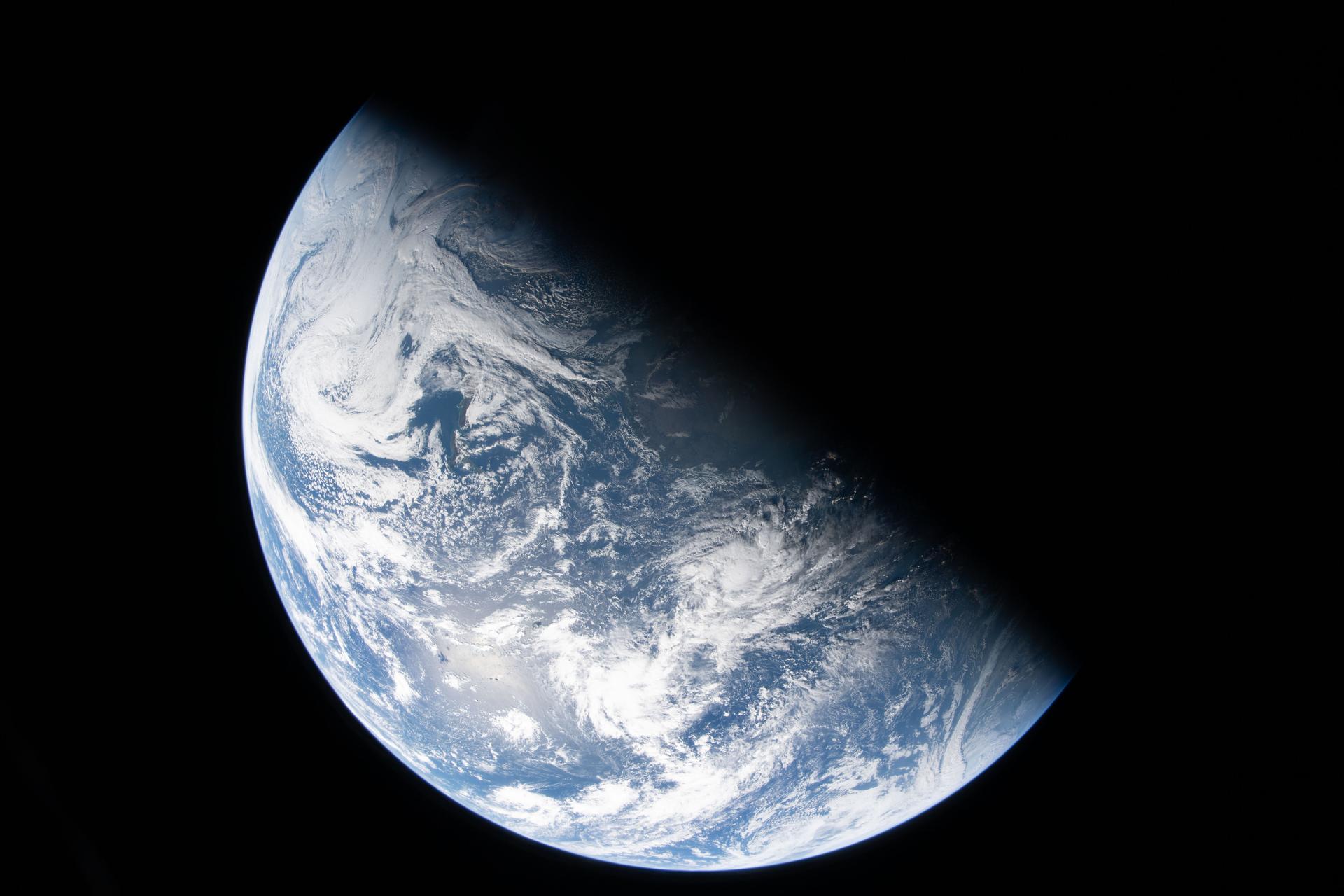 A close up of Earth in space, its top half cut diagonally in shadow, with only the bottom half illuminated.