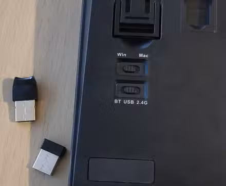 A Bluetooth / USB / 2.4G switch on the back of a keyboard along with a USB and 2.4GHz dongle.