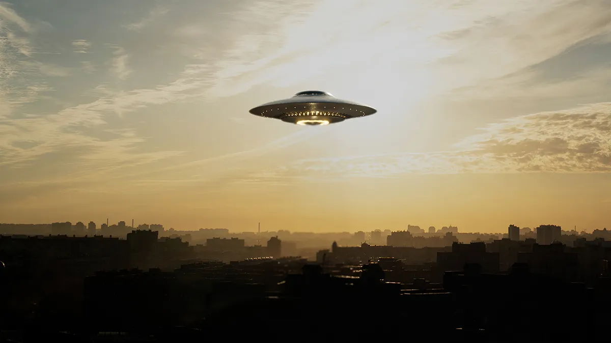A UFO hovering over land in a cloudy sky
