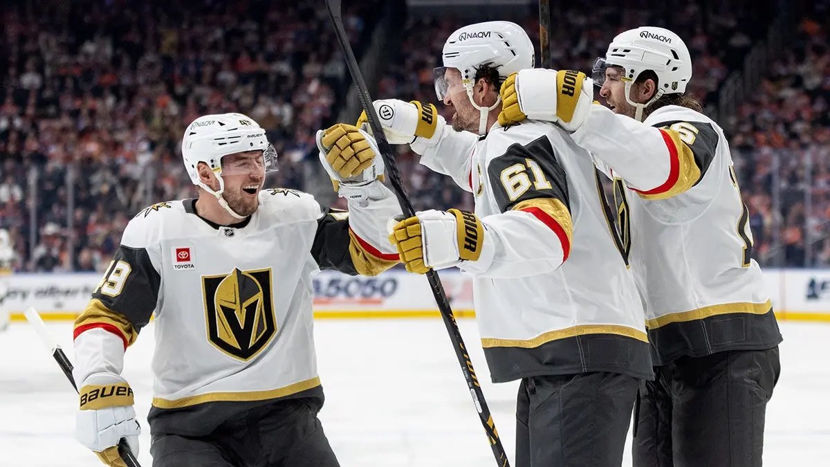 Vegas Golden Knights players Ivan Barbashev, Mark Stone, and Noah Hanifin celebrating a goal on ice.