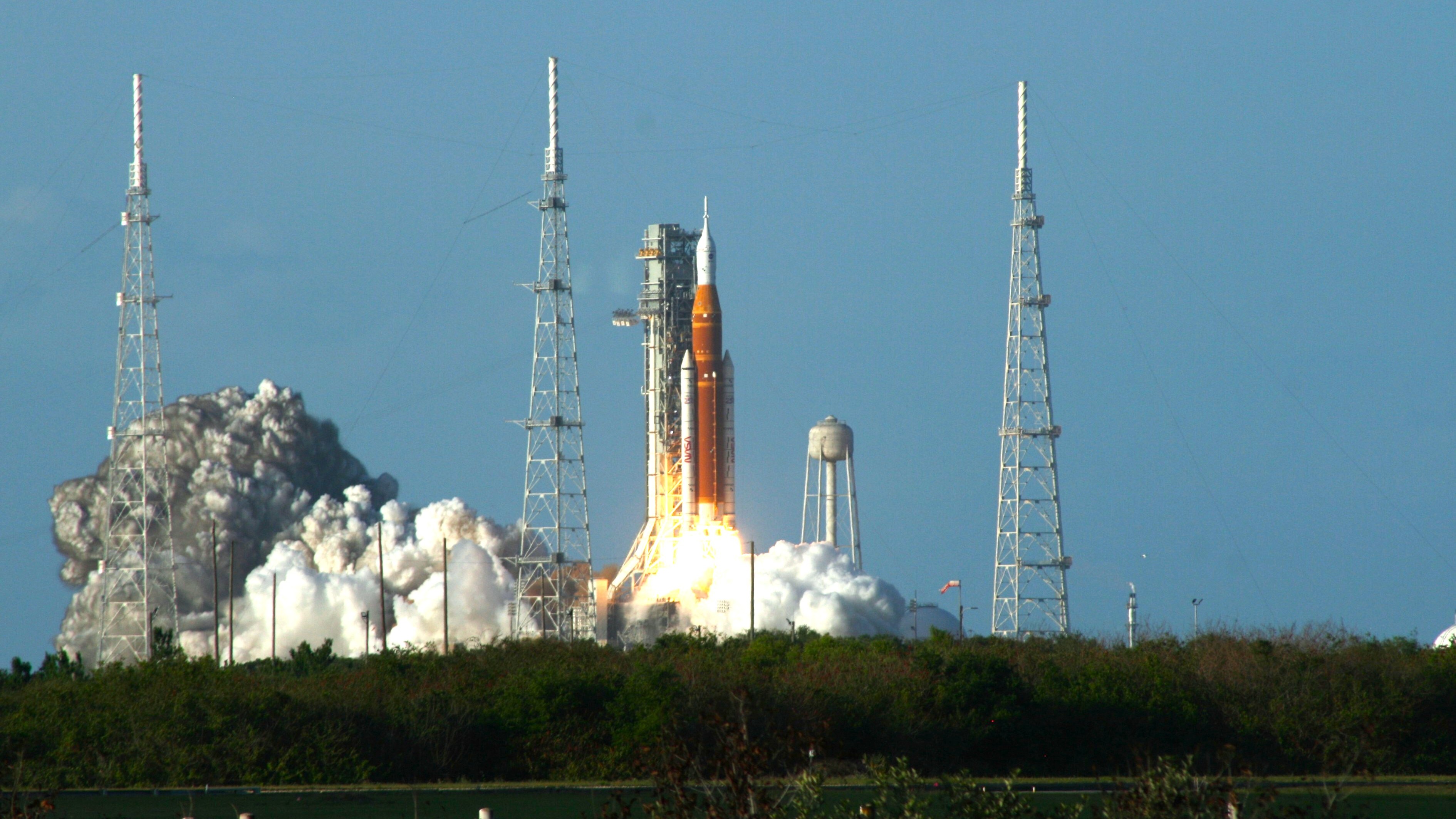 Artemis II rocket lifts off behind a row of shrubbery.
