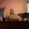 Ken Warner is pictured at his desk, a large computer monitor is visible. His cat is on the desk, looking at the camera. 