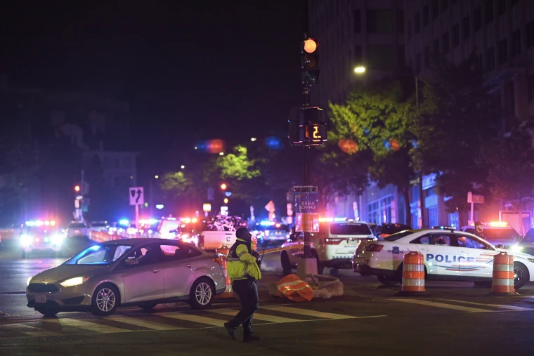 Red and blue lights atop law enforcement vehicles illuminate a city streetscape at night.