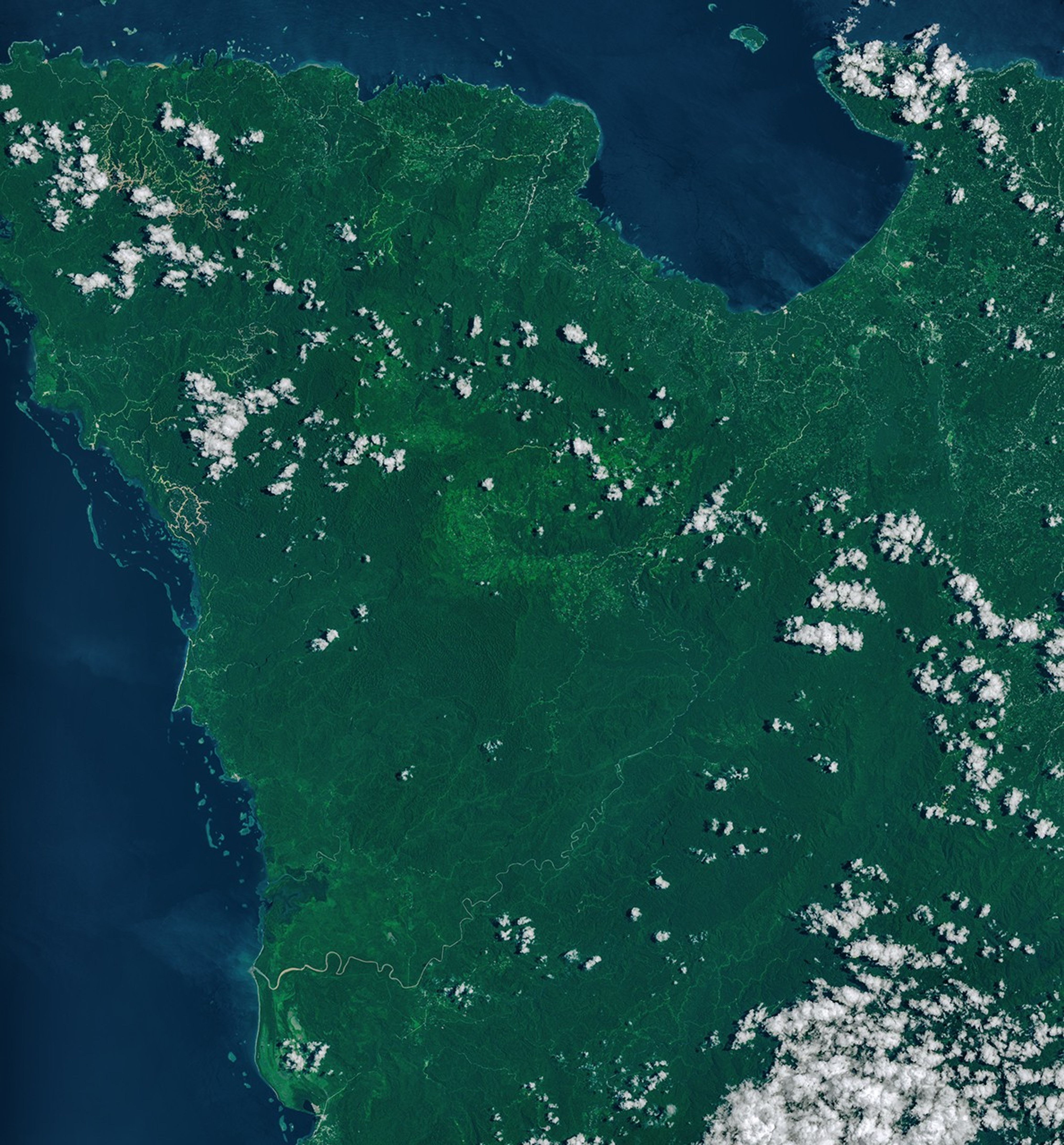 A narrow, light-brown landslide scar cuts through dark green forested mountains in East New Britain and extends south toward a stream valley. Rivers swollen with floodwaters, areas of forest clearing, and scattered clouds are also visible in some parts of the image.